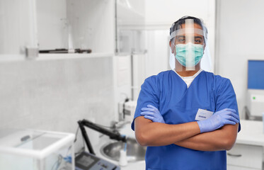 Fototapeta na wymiar medicine, healthcare and protection concept - indian doctor or male nurse in blue uniform, protective medical mask and face shield over laboratory or hospital background