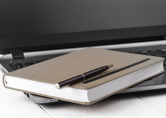 Orange notebook with a pencil lying on a laptop