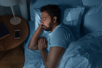 people, bedtime and rest concept - indian man sleeping in bed at home at night