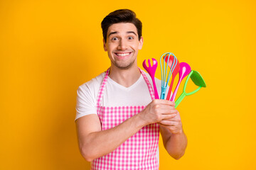 Portrait of cheerful person arms hold cook equipment toothy smile look camera isolated on yellow color background
