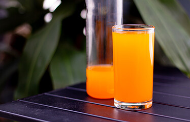 A fruit juice or orange juice drink in a glass made from oranges is a naturally sweet, juicy, fresh fruit, placed on a black chair outside.