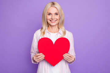 Photo of sweet charming mature woman dressed pink shirt holding big paper heart isolated purple color background