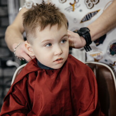 Cute little boy of five getting a haircut in a barbershop. The hairdresser does the baby's hair. Barber shop. Childhood. A new hairstyle for a little boy.