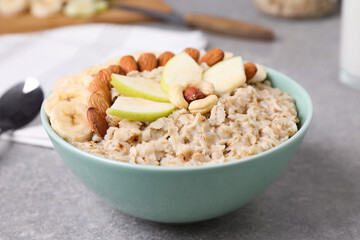 Bowl of delicious oatmeal with fruits and nuts on grey table
