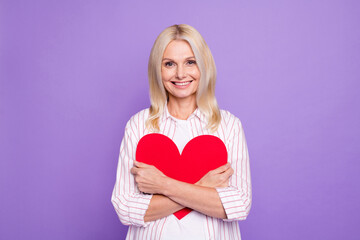 Photo of shiny adorable lady pensioner wear striped shirt hugging big paper heart isolated violet color background