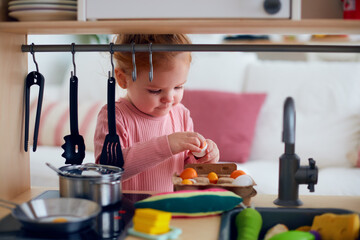 cute toddler baby girl playing on toy kitchen at home, pretends frying eggs