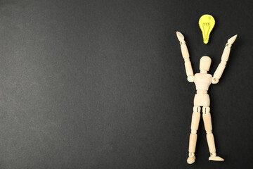 Wooden puppet and paper lightbulb on black background, flat lay. Space for text