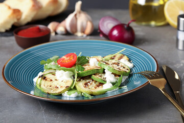 Delicious grilled zucchini slices served with cottage cheese and tomatoes on grey table, closeup