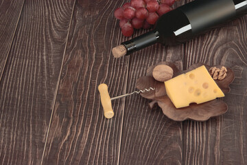 Expensive bottle of wine and corkscrew, grapes and cheese lie on the background of wooden boards