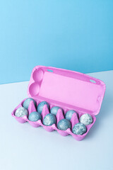 Purple egg packaging with painted blue Easter eggs on light blue background.
