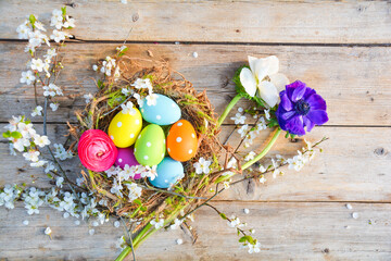 Easter basket with eggs and spring flowers on a rustic wooden background - nest with colored eggs -...