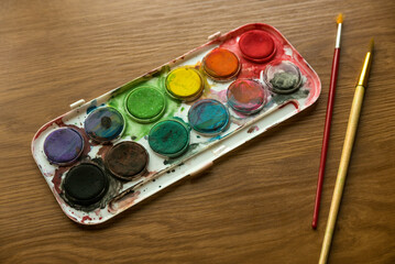 Selective focus of watercolor palette with brush on wooden background.