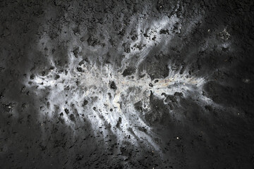 Artistic, abstract high contrast image: bright oil spill on dark concrete form like infection, cancer or pollution spreading; color photo.
