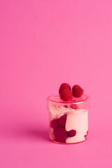 a freshly prepared spring dessert of raspberries and quark with cream in a pink glass on a pink background
