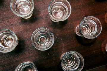 Shot glasses with palinka, brandy, vodka or any transparent liquid on brown table. Illustration picture for party or alcoholism; color photo.