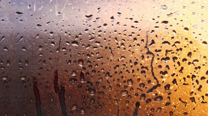 Horizontal natural background with water drops on the window with sunbeams, condensation on the glass with dripping drops