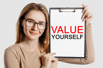 value yourself. Beautiful young business woman wearing glasses holds a clipboard with mock up space isolated on gray background