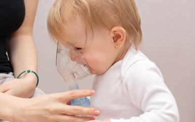 Little toddler girl with asthma and allergies makes inhalation in a mask with medication through a...