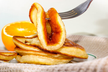 A pile of fried pancakes on a saucer with citrus fruits in the background.