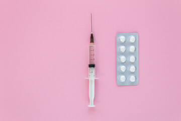 Top view of medical syringe with white pills on pink background, health and vaccination concept....