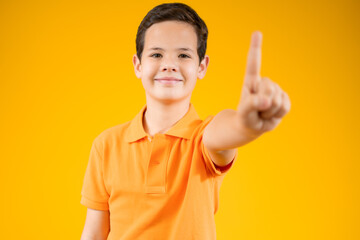Happy young boy in casual t-shirt pointing up and looking at the camera over orange background