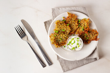 Potato pancakes or draniki with sour cream in plate on marble background. Top view.