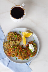 potato pancakes or draniki with sour cream in plate and coffee on marble background. Top view.