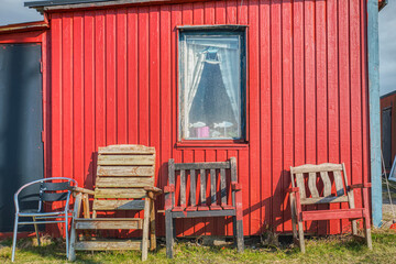 Traditional Scandinavian summerhouse facade with a rectangular window and old chairs against the red wooden exterior made of planks. Fish decoration suggests it's a Swedish fisherman hut, summer house