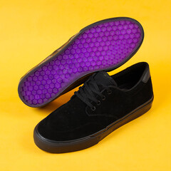 Plain black sneakers with a purple base. Plimsoll shoes on a yellow background give a bright effect to the photo. Front shot. Side shot. Hands holding sneakers through yellow paper background.