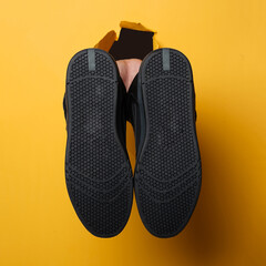 the man's right hand holding a pair of shoes through the yellow paper background. Copy space for ad content. Best choice concept. Holes in wall paper. Mock Up of creative advertising space. Sneakers.