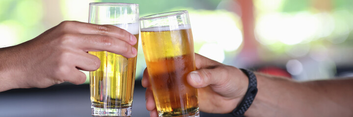 Two male hand hold glass of cold beer and clink glasses. Spending time in male company in bar.