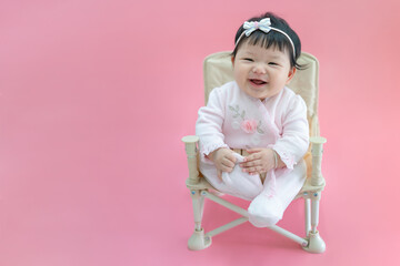 Asian happy baby smiling and sitting on a chair in pink color background. Cute 6 months baby wearing pink cloth with copy space use as concept of valentine, love, baby or kid department in hospital.