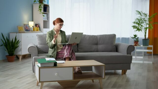 young businesswoman in jacket and pajamas talks by video call on laptop while working online while sitting at home on couch during quarantine
