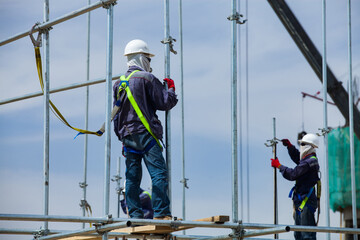 Industrial climbers assembling construction scaffolds. On blue sky background. Focus on foreground.