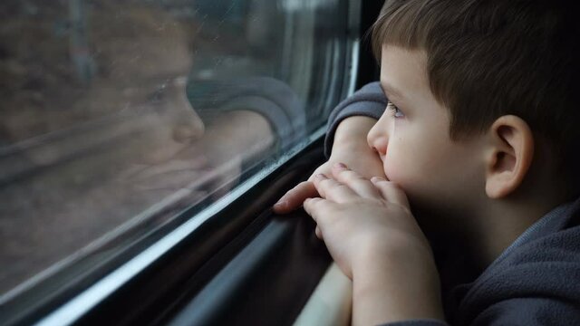 sad little boy rides the train and looks out the window.