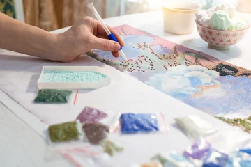 home hobby-to draw pictures of rhinestones, multi-colored diamond mosaic. the process of gluing pencil rhinestones on canvas pictures of the house on the table with tea and nuts © Taranova_ksenya