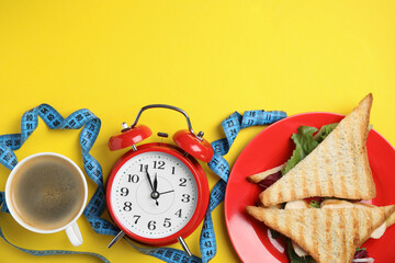 Flat lay composition with tasty sandwiches and alarm clock on yellow background, space for text....