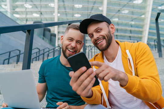 Two friends sitting on football stadium steps and using online betting service on their laptop