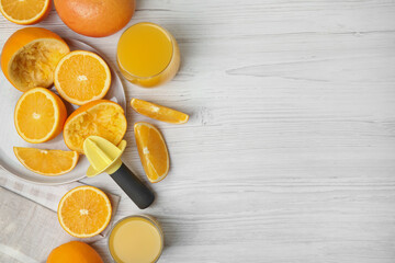 Fresh oranges, reamer and juice on white wooden table, flat lay. Space for text