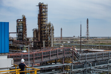 Fototapeta premium Panorama view of oil refinery plant. Distillation columns and pipes. Gas torch masts. Worker in white hardhat on foreground.