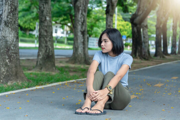 Portrait of young Asian woman enjoying and relaxing outdoors. Cheerful teenage female sitting on the road in the park on a sunny summer day.