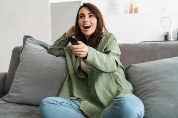 Happy young woman watching tv on sofa