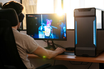 Caucasian brunette guy in headphones playing video game on his computer