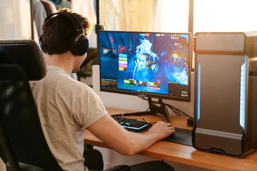 Fotobehang Caucasian brunette guy in headphones playing video game on his computer © Drobot Dean
