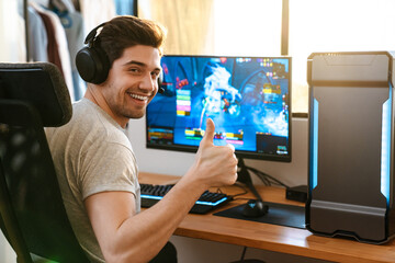 Happy guy in headphones showing thumb up while playing video game