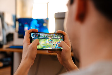 Unshaven brunette guy playing video game on his mobile phone