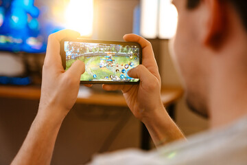 Unshaven brunette guy playing video game on his mobile phone - obrazy, fototapety, plakaty