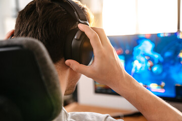 Caucasian brunette guy in headphones playing video game on his computer