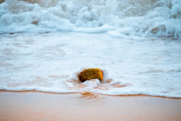 Single big rock on a sandy beach and sea waves hitting it