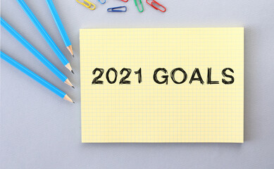 2021 GOALS text in notebook on gray background next to pencils and paper clips.